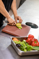 Professional chef in uniform preparing fresh vegetables on cutting board in restaurant kitchen. Culinary concept