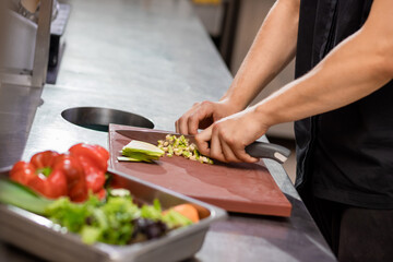 Professional chef in uniform preparing fresh vegetables on cutting board in restaurant kitchen. Culinary concept