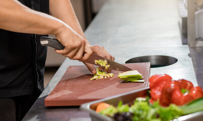 Obraz na płótnie Canvas Professional chef in uniform preparing fresh vegetables on cutting board in restaurant kitchen. Culinary concept