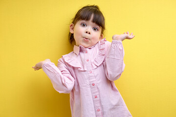 misunderstanding child girl shrugging, i don't know concept. isolated yellow background, portrait...