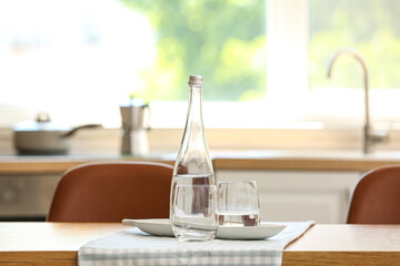 Bottle of water with glass, stand and napkin on table in kitchen