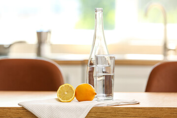 Bottle of water with glass, lemon and napkin on table in kitchen - Powered by Adobe