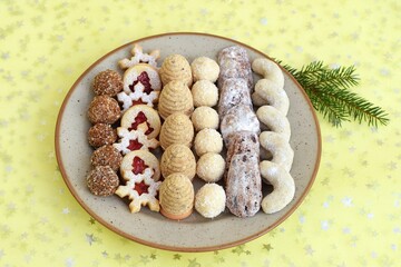 Various kinds of Christmas cookies arranged on a plate, with spruce twig decoration