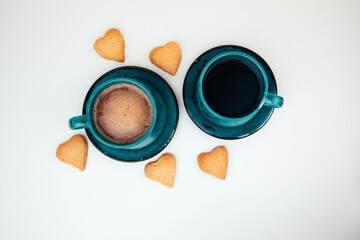 Two mugs of coffee with foam and a plate with heart-shaped shortbread cookies on a white background. Tpo view