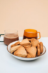 Two mugs of coffee with foam and a plate with heart-shaped shortbread cookies on a white-beige background. Front view