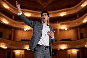 Theatre play a young actor in original image. Sincere emotions transmitted camera. Photo for cultural and fashion magazines, posters and websites. Brunette male in gray suit singing, gesturing