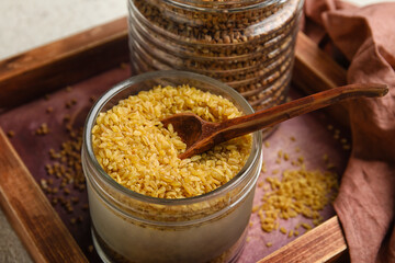 Wooden board with jar of bulgur on table, closeup