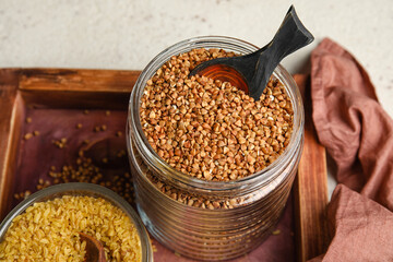 Wooden board with jar of buckwheat on table, closeup