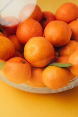 Orange mandarins clementine with green leaves in round clear vase close up. Front view