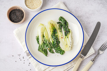 Plate of tasty stewed pak choi cabbage and sesame seeds on light background