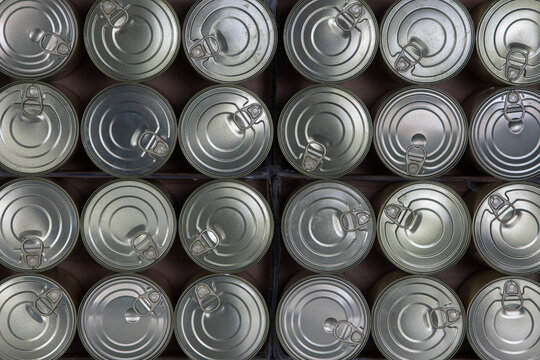 Food behind sheet metal. Lined up tin cans with pull-off lids viewed from above.