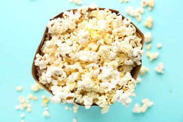 Paper bag with delicious popcorn on color background
