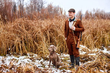 male hunter in suit with dog posing looking at side outdoors in nature, with rifle, looking for...