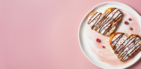 Valentine's day banner on pink background. Heart shaped toasts drizzled with chocolate and cream, sprinkled with dried raspberries. Morning romantic breakfast.