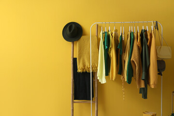 Rack with stylish female clothes and accessories near yellow wall