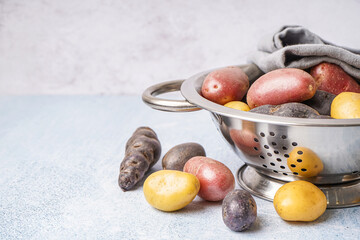 Colander with different raw potatoes on light background