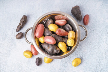 Colander with different raw potatoes on light background
