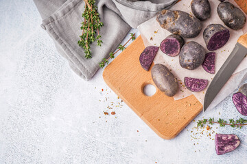 Wooden board with raw purple potatoes and thyme on light background