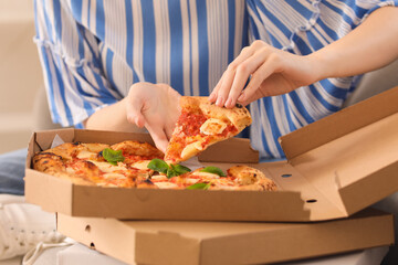 Young woman taking slice of tasty pizza from box at home, closeup