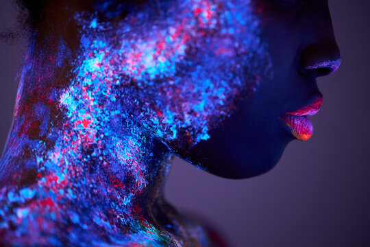 Body art glowing in ultraviolet light, close-up face of black woman with big lips, fluorescent body art isolated on purple studio background. futurustic, fashion, people, models concept