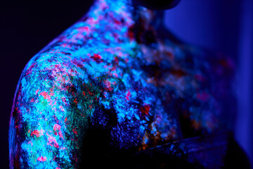 Close-up photo of black female skin with fluorescent paintings, body art make-up. cropped unrecognizable lady with art on skin lighted on ultra violet space. art, fashion concept