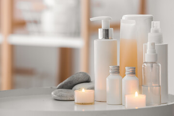 Cosmetic products with spa stones and burning candles on table in salon, closeup