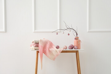 Vase with tree branches, Christmas balls and sweaters on table near light wall