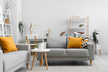 Interior of living room with grey sofas, coffee table, workplace, shelving units and bicycle near grey wall