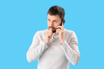 Handsome man biting nails and talking by mobile phone on blue background