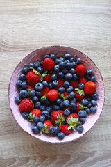 Pink rustic bowl filled with fresh blueberries and strawberries. Wooden background, top view.