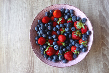 Pink rustic bowl filled with fresh blueberries and strawberries. Wooden background, top view.