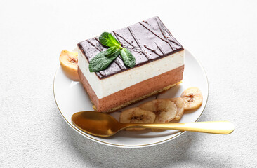 Plate with piece of birds milk cake, mint leaves, dried banana slices and spoon on white background