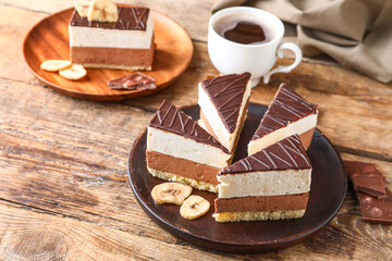 Plates with pieces of birds milk cake, dried banana slices, chocolate and cup of coffee on wooden background