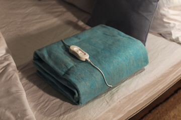 Fototapeta na wymiar Folded electric heating pad with controller on bed at night, closeup