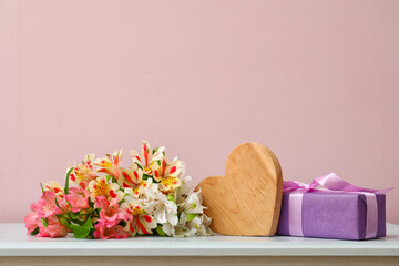 Bouquet of beautiful alstroemeria flowers, wooden heart figure and gift box on table near color wall. Mother's day celebration