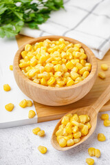 Cutting board with spoon and bowl of canned corn kernels on white table