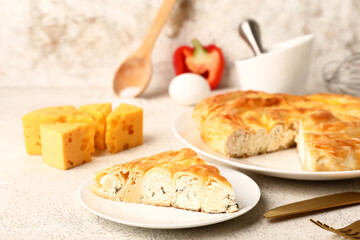 Plate with piece of delicious cheese pie and ingredients on white table