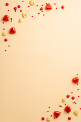Valentine's Day concept. Top view vertical photo of heart shaped chocolate candies sprinkles and golden hearts on isolated pastel beige background with copyspace