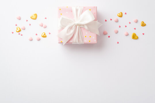 St Valentine's Day concept. Top view photo of big pastel pink gift box with satin ribbon bow golden hearts and sprinkles on isolated white background with copyspace