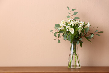Vase with bouquet of beautiful alstroemeria flowers and eucalyptus branches on table near color wall