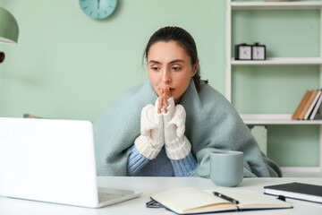 Frozen young woman working with laptop at home