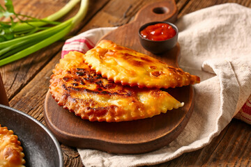 Cutting board with tasty chebureks and sauce on wooden background