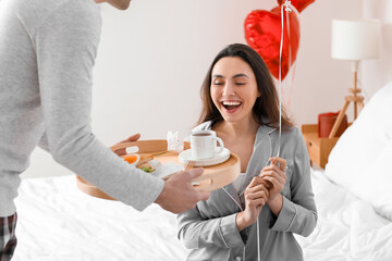 Young man bringing his wife breakfast in bed on Valentine's Day