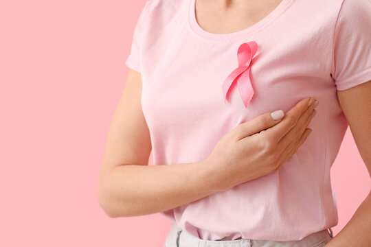 Young woman in t-shirt with pink ribbon on color background, closeup. Breast cancer awareness concept
