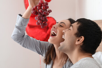Young couple eating grapes in bedroom on Valentine's Day, closeup