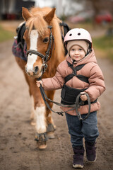 Little girl in protective jacket and helmet with her brown pony before riding Lesson