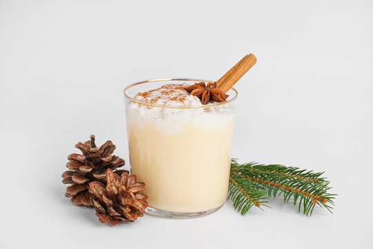 Glass of tasty eggnog cocktail, fir branch and cones on white background