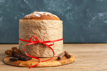 Board with Panettone, fir cones, chocolate and cinnamon on table near dark wall