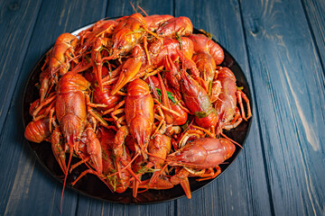 Boiled crayfish in a black plate on a black wooden background. Lots of boiled crayfish.