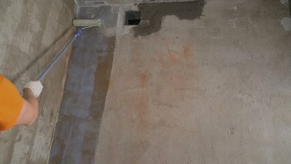 A worker applies a primer to a wall with a long-handled roller. A man's hand applies a primer on a...
